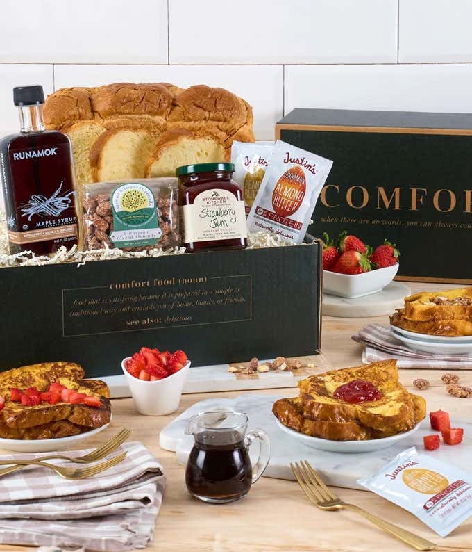 In the background, a loaf of brioche, with a bottle of syrup. In the foreground, a cup of tea, tea chest, a jar of chocolate hazelnut spread, and the finished product of brioche french toast,all on a wooden tray.