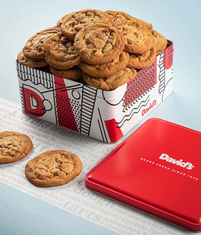 A decorative tin filled with David's peanut butter cookies. The tin features a red, white, and black design with the David's logo. A few cookies and the red lid are placed beside the tin.