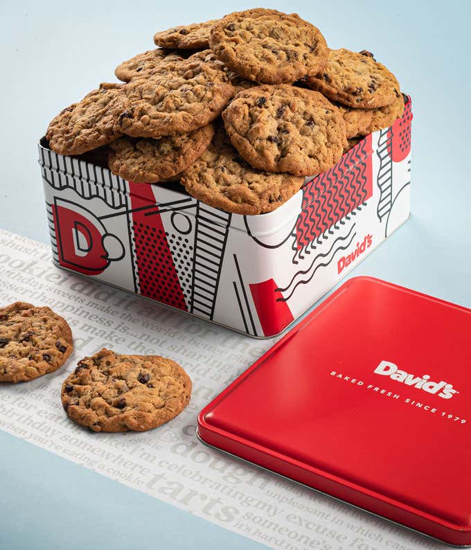  A decorative tin filled with David's oatmeal raisin cookies. The tin features a red, white, and black design with the David's logo. A few cookies and the red lid are placed beside the tin.