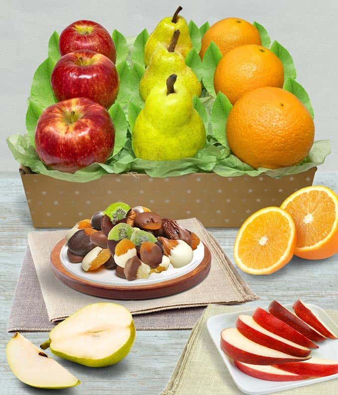 Gift box containing fresh apples, pears, and oranges, accompanied by a plate of assorted chocolate-dipped dried fruits and nuts, with sliced fruit displayed in the foreground.