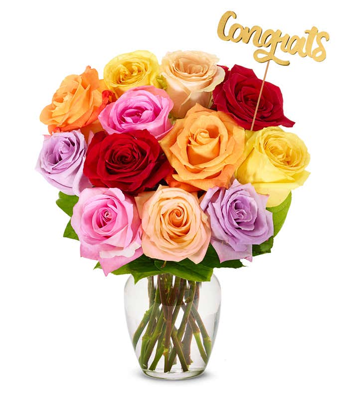 Bouquet of one dozen vibrant rainbow roses with optional elegant glass vase and personalized gift message for a housewarming.