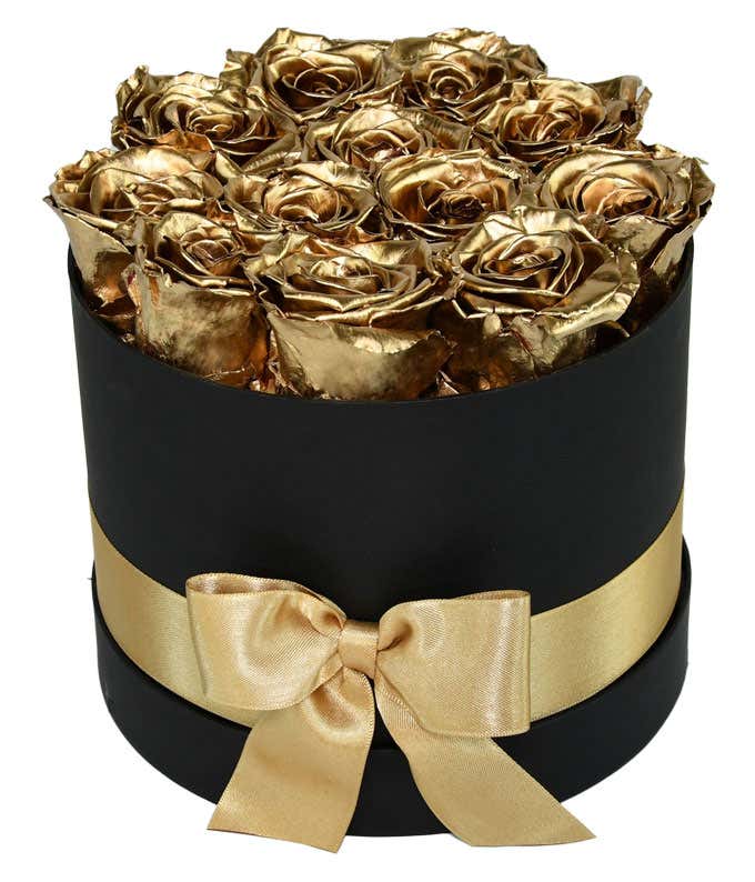 One dozen gold preserved roses arranged in a black hat box with a gold ribbon.