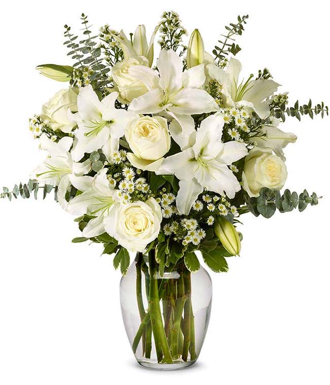 An elegant floral arrangement featuring white roses, white lilies, white asters, and eucalyptus, optionally displayed in a glass vase.