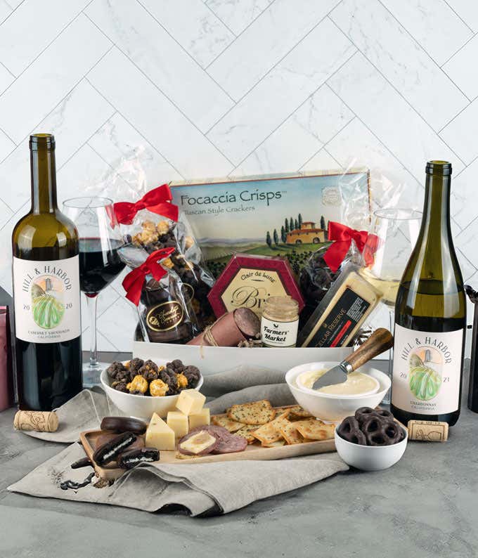 Gourmet gift box featuring focaccia crisps, brie cheese, cheddar cheese, summer sausage, mustard, chocolate-covered snacks, a bottle of Hill & Harbor Cabernet Sauvignon, and a bottle of Hill & Harbor Chardonnay, with glasses of red and white wine, and an 