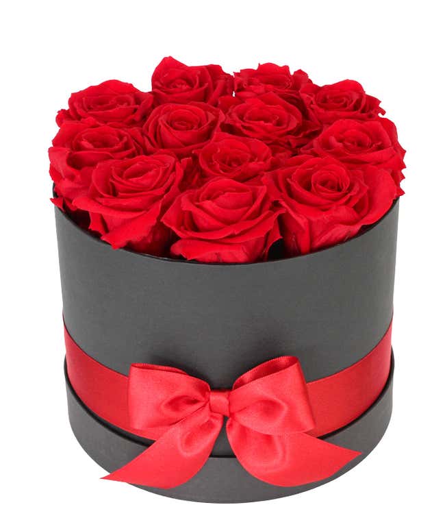 Arrangement of vibrant red roses in a round black box, adorned with a red satin ribbon tied into a bow.