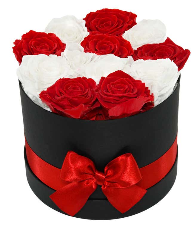 Elegant arrangement of red and white roses in a black round box, adorned with a red satin ribbon and bow, creating a sophisticated and romantic floral gift.