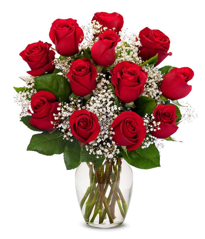 a bouquet of 12 red roses with small white flowers and greenery in between in a clear glass vase