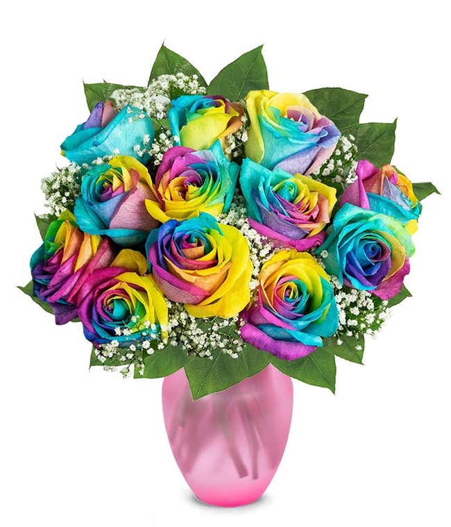 A colorful bouquet of rainbow roses in a clear glass vase, with petals in vibrant hues of blue, yellow, pink, and purple, accented by baby's breath and green leaves, creating a bright and cheerful display.