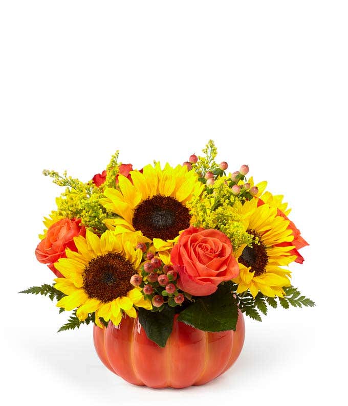 A cheerful floral arrangement featuring sunflowers, orange roses, yellow solidago, and peach berries, all beautifully arranged in a pumpkin container.