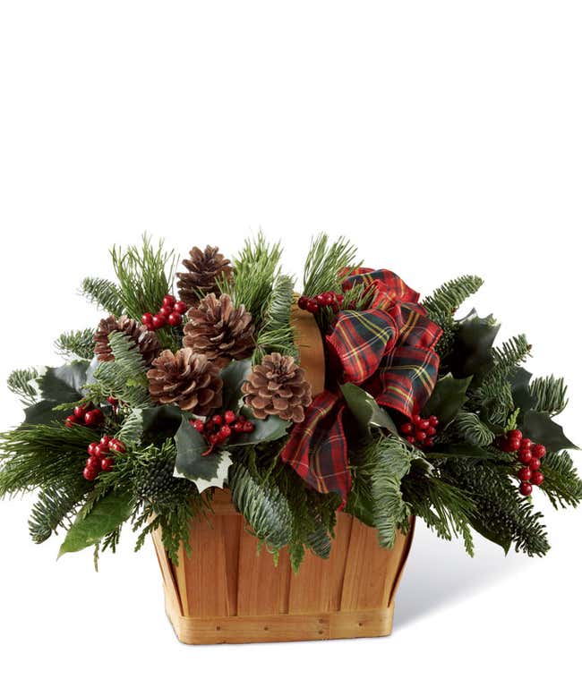 A festive arrangement with holly, assorted evergreens, pinecones, and salal, displayed in a keepsake basket.