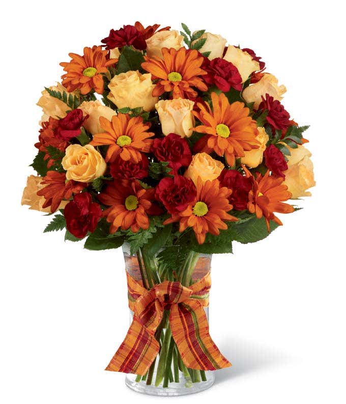 A delightful floral arrangement featuring peach spray roses, burgundy mini carnations, and butterscotch daisy poms, adorned with a plaid ribbon decoration, all elegantly presented in a vase.