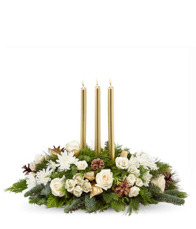 A festive arrangement with ivory roses, ivory spray roses, white poms, pinecones, assorted evergreens, and three gold taper candles