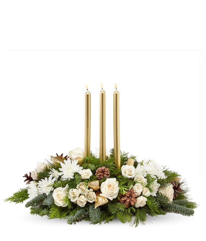 A festive arrangement with ivory roses, ivory spray roses, white poms, pinecones, assorted evergreens, and three gold taper candles