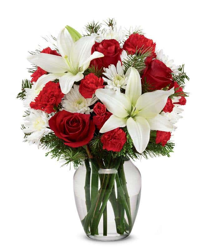 A festive arrangement with red roses, white lilies, red carnations, red mini carnations, and white poms.