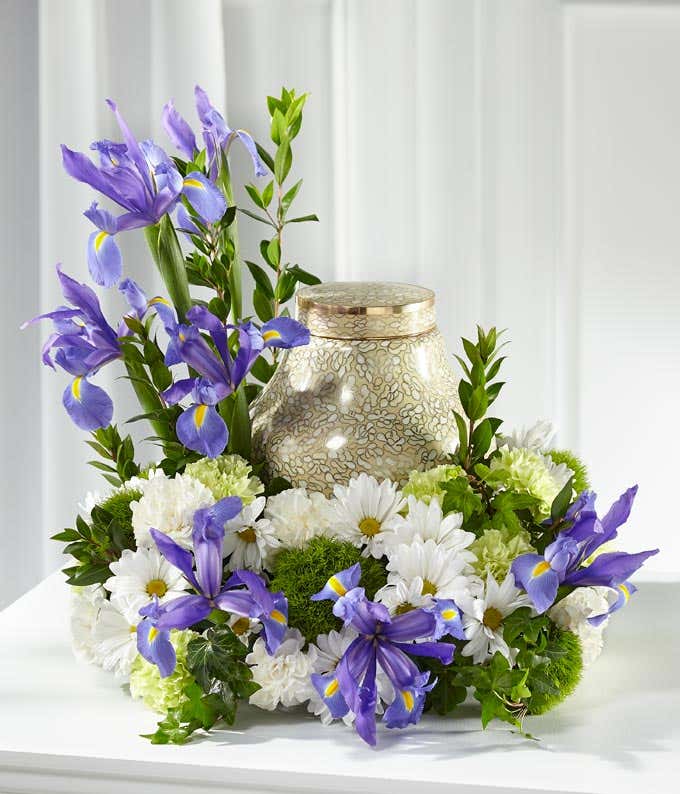 blue, white and green flowers wrapped around a gold urn sitting on a white table with white background