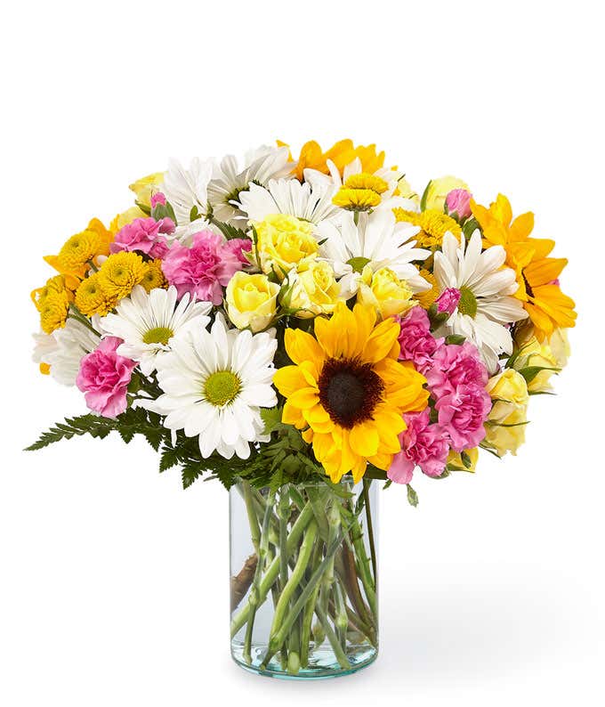 Sunflowers, white daisies, yellow spray roses, pink carnations, and fresh greens, arranged into a mason jar