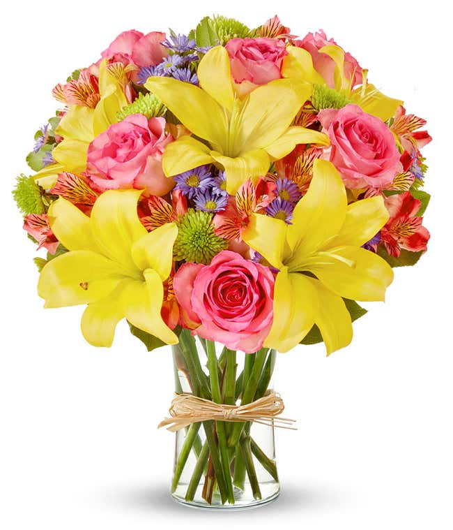 A vibrant arrangement featuring yellow lilies, pink roses, pink alstroemeria, green poms, and purple Monte Casino, beautifully arranged in a glass vase. This colorful mix offers a cheerful and eye-catching display, perfect for brightening any occasion.