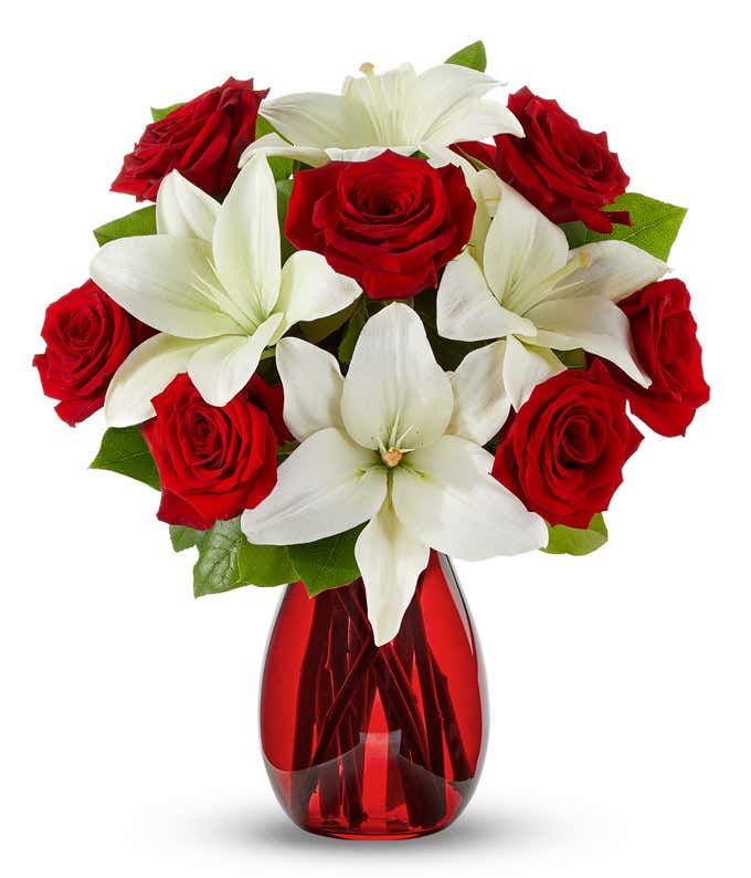 A floral arrangement featuring red roses and white lilies in a red cylinder vase.