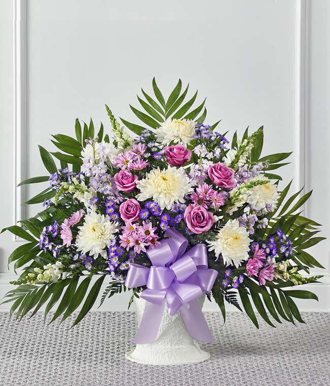 A heartfelt sympathy floor basket featuring white roses, white snapdragons, lavender stock, lavender mums, and white Monte Casino. This elegant and serene arrangement offers a comforting and respectful tribute. 