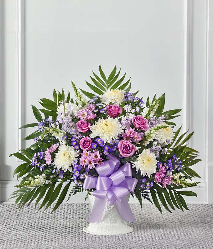 A heartfelt sympathy floor basket featuring white roses, white snapdragons, lavender stock, lavender mums, and white Monte Casino. This elegant and serene arrangement offers a comforting and respectful tribute. 