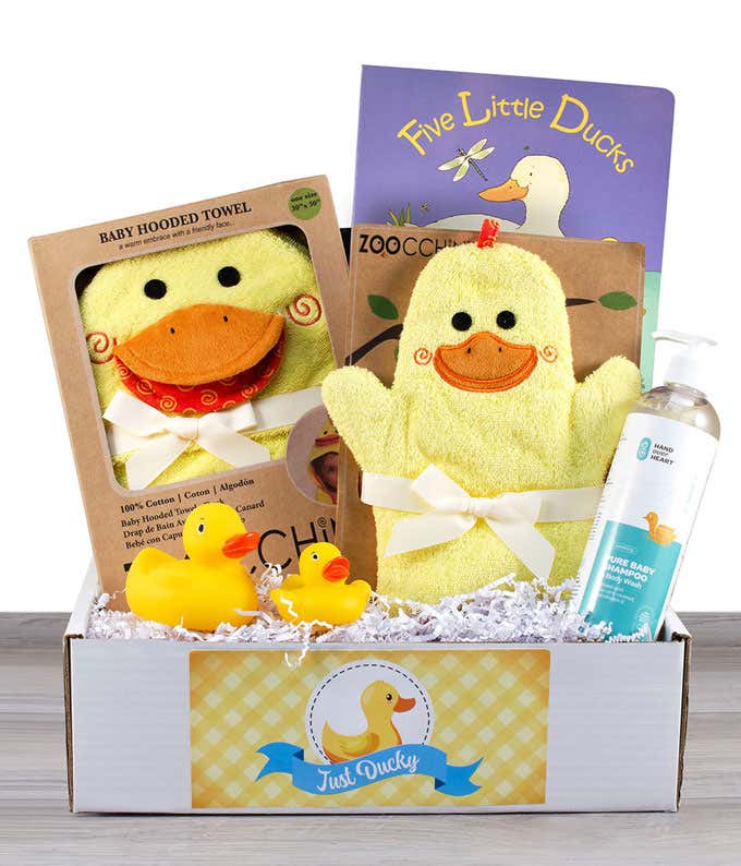 A bright yellow box containing a duck hooded towel, a duck hand puppet, a bottle of baby shampoo, two rubber duck toys, and a book titled 'Five Little Ducks'.