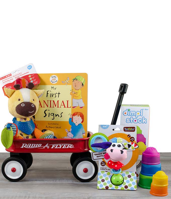 A red Radio Flyer wagon filled with a plush cow, interactive rattles, a colorful stacking toy, and other playful items.