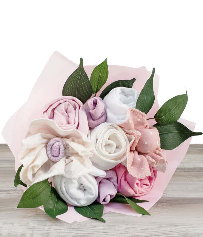 A pink flower bouquet made from rolled baby clothing items, including onesies, socks, and wash clothes, with fake greenery, wrapped in pink paper.