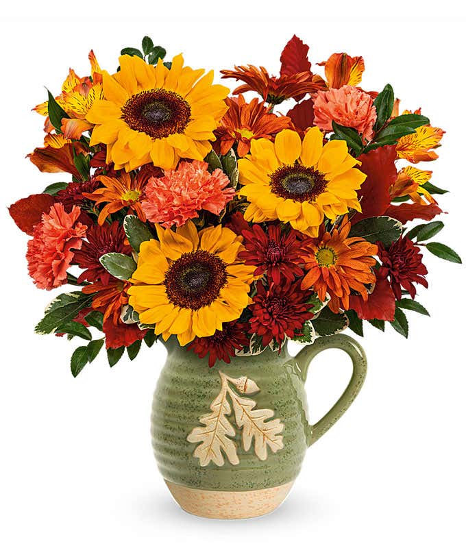 A cheerful floral arrangement featuring yellow sunflowers, orange carnations, orange alstroemeria, bronze daisy spray chrysanthemums, bronze cushion spray chrysanthemums, huckleberry, variegated pittosporum, and burgundy copper beech, all beautifully disp