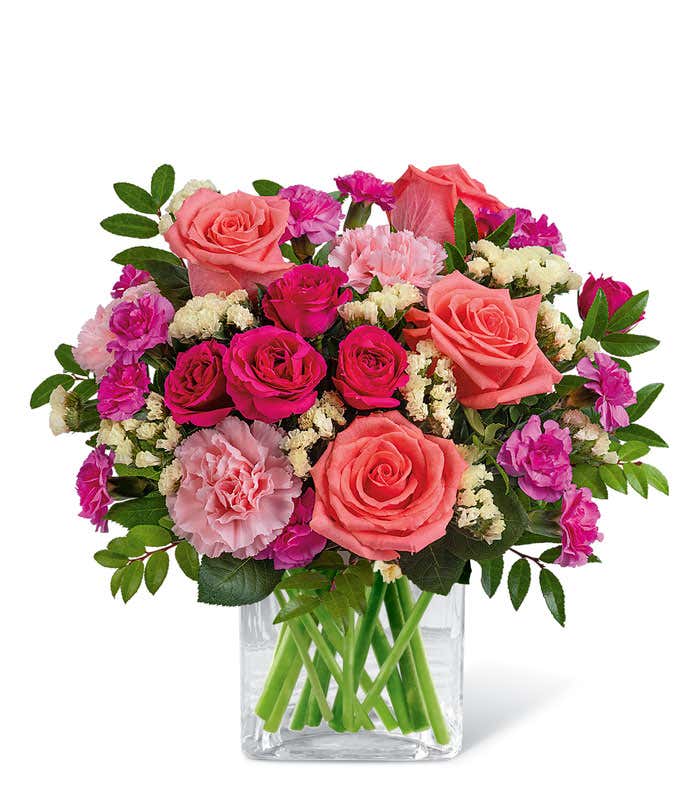 Short, round bouquet of coral, pink, and yellow flowers in a Clear Glass Cube Vase