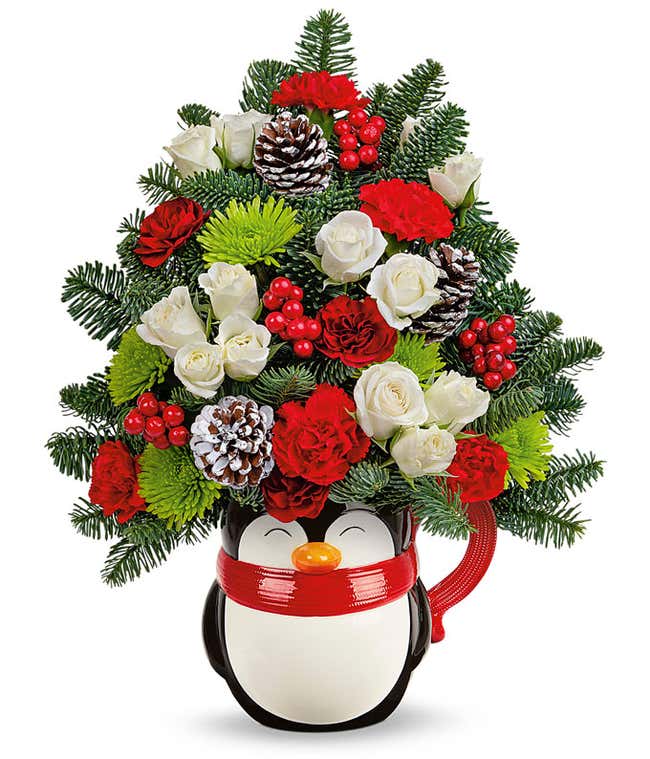 A festive arrangement with premium red roses, deluxe and premium white roses, mini maroon and red carnations, green cushion chrysanthemums, white button chrysanthemums, floral greens, pinecone and red berry details, in a keepsake penguin mug vase.