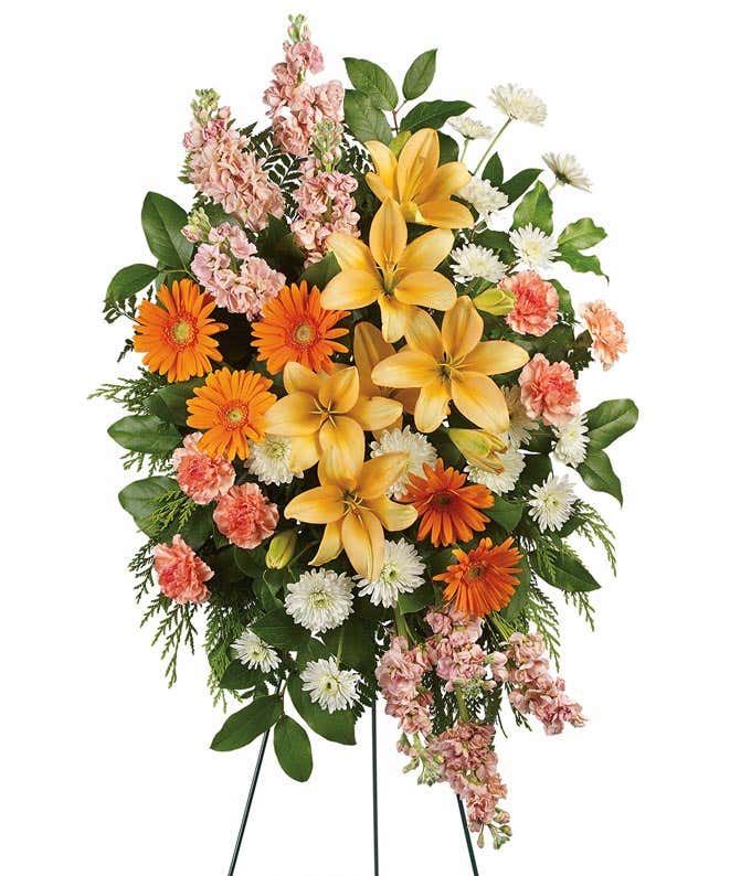 A standing funeral spray featuring Peach Asiatic Lilies, Orange Gerberas, Orange Carnations, Peach Stock, White Cushion Chrysanthemums, and Floral Greenery, offering a serene tribute of comfort and solace during a time of loss.