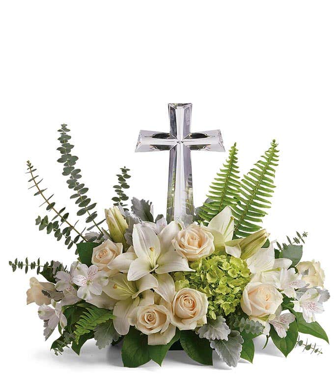 An arrangement of white asiatic lilies, creme roses, and white alstromeria with floral greens and a crystal cross