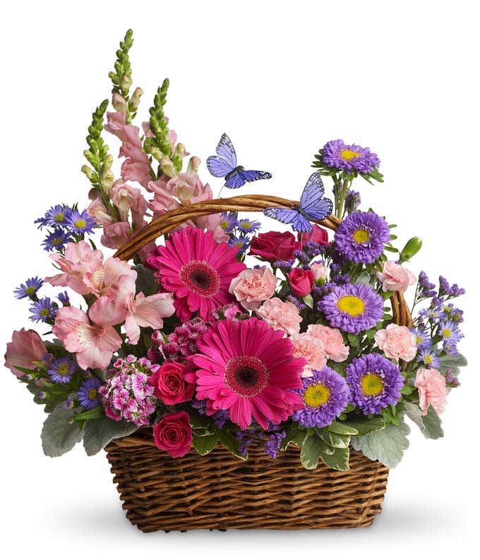 Floral arrangement featuring pink snapdragons, pink mini carnations, pink alstroemeria, purple Matsumoto asters, hot pink gerbera daisies, in a woven handled basket.