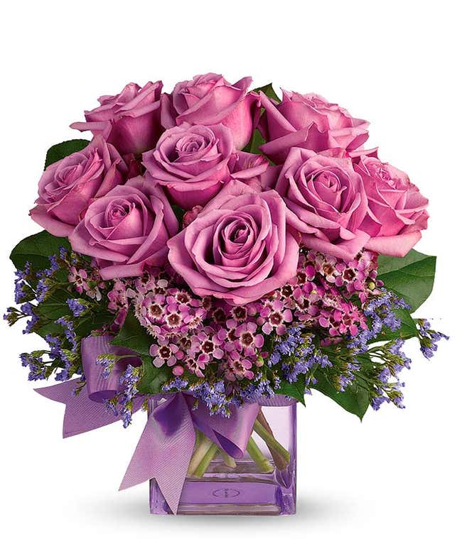 A striking arrangement featuring purple roses, seasonal greens, elegantly presented in a square glass vase adorned with a purple ribbon. This beautiful combination offers a luxurious and sophisticated display, perfect for any special occasion.