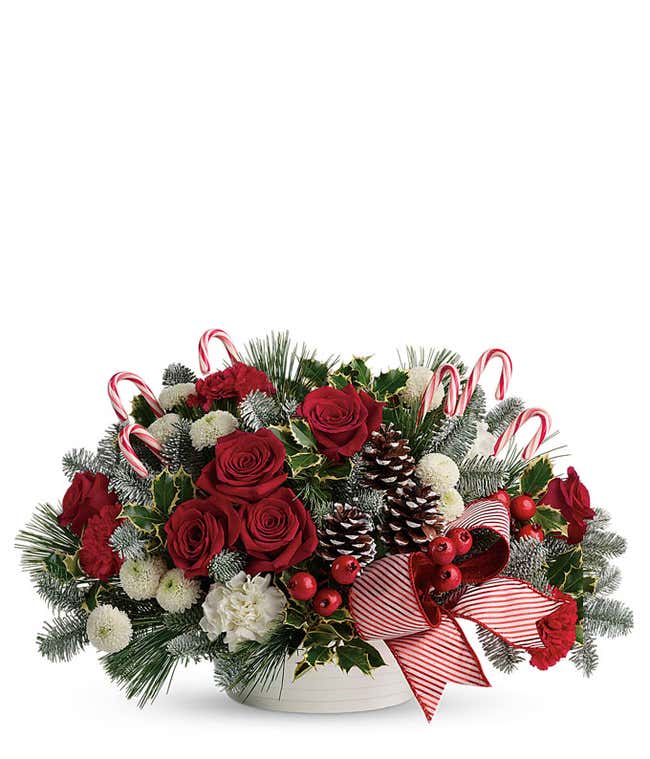 A festive arrangement with red roses, red carnations, white carnations, white button spray chrysanthemums, variegated holly, noble fir, white pine, and candy canes.