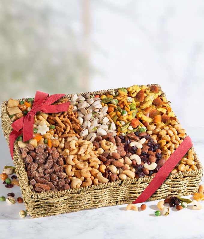 A woven basket filled with an assortment of snacks including almonds, pistachios, pretzels, dried fruits, and various nuts, all neatly arranged and tied with a red ribbon