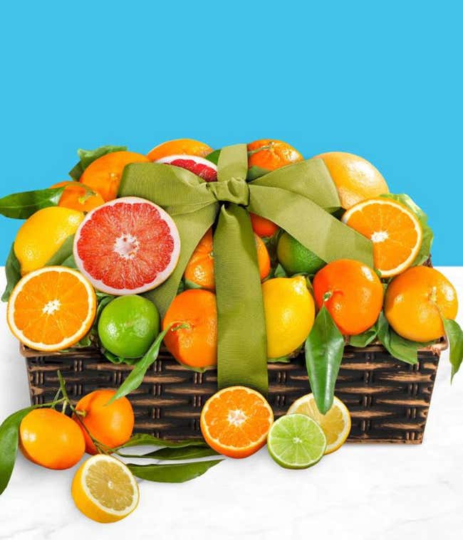 A basket brimming with fresh citrus fruits including oranges, grapefruits, lemons, and limes, decorated with a large green ribbon. 