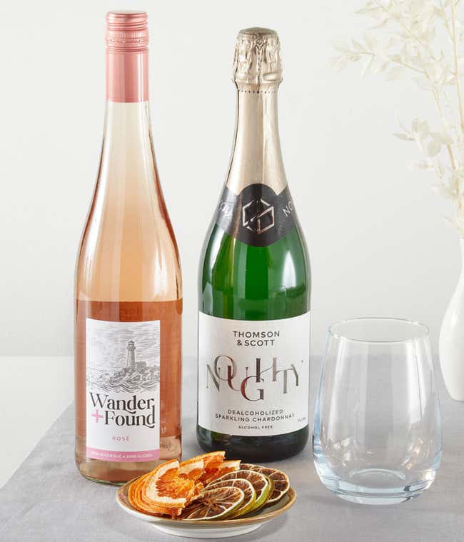 A bottle of non-alcoholic ros&eacute; and a bottle of alcohol-free sparkling juice, with a glass and a plate of dried fruit slices.